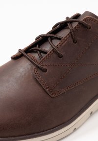 Bruna läderskor med en slät yta, rund tå och snörning med bruna snören och kontrasterande beige sula.