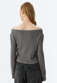 Grauer gerippter Strickpullover mit einem schulterfreien Design, langen Ärmeln und einem cropped Saum. Verfügt über rohe Kanten und einen strukturierten Stoff.