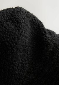 Černá texturovaná tkanina s měkkým, hebkým povrchem. Materiál vypadá chlupatě a silně, vykazuje bohatou, tmavou barvu.