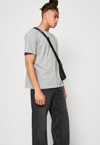 Grå bomulls T-skjorte med korte ermer, med en liten logo på brystet. Brukes med løse, mørke jeans og en svart crossover-veske.