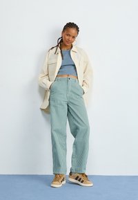 Light beige oversized button-up shirt over a gray crop top, paired with teal-striped high-waisted pants and brown sneakers with black stripes.
