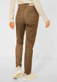 Bruna kordbyxor med smal passform och bakfickor. Har en subtil textur och en CECIL-märke på midjan. Bärs med ljusa sneakers.