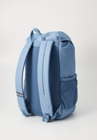 Blue backpack with mesh siding, padded straps, and a top handle. Features a side pocket and a smooth, durable fabric finish.