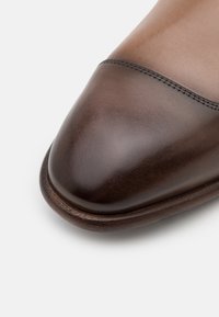 Chaussure habillée en cuir marron avec un bout rond, affichant une texture lisse et une couture sur le dessus. Semelle en cuir avec un léger brillant.