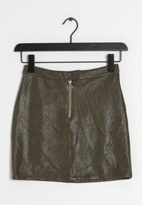 Mini-jupe vert olive avec un motif texturé en imprimé serpent, dotée d'une fermeture éclair à l'avant et d'un détail de tirette en anneau, accrochée à un cintre noir.