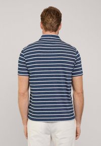 Granatowa koszulka polo z krótkim rękawem w białe poziome paski, z kołnierzykiem i strukturalną tkaniną. Widok z tyłu pokazuje detale szycia.