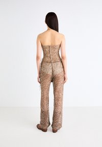 Strapless, form-fitting jumpsuit in bronze with sequin embellishments and a sheer finish, featuring side ties and flared legs.