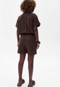 Bruine korte mouwen romper met kraag, voorzien van een elastische taille en losse pasvorm, met een plooi-detail aan de achterkant. Soepele stof met een ontspannen ontwerp.