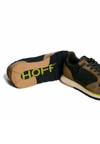 Zapatillas con un upper negro, detalles de ante marrón y un logo verde. Suela de goma gruesa con un patrón de textura.