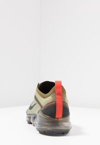 Nike Air VaporMax in verde oliva e nero, presenta una parte superiore testurizzata, un anello sul tallone rosso e una suola di ammortizzazione ad aria trasparente.