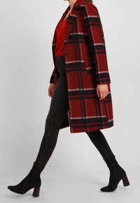 Cappotto di lana a quadri rossi e neri con maniche lunghe e colletto a revers, abbinato a jeans skinny neri e stivaletti neri con tacco a blocco.