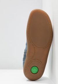 Semelle d'une chaussure bleue avec une semelle extérieure en caoutchouc marron, logo circulaire vert avec une grenouille, et texte espagnol en relief autour des bords.