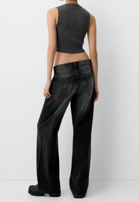 Svarta vida jeans med en urtvättad finish och två bakfickor. Kombinerat med en mörkgrå ribbad ärmlös topp.