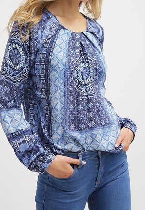 Blaue gemusterte Bluse mit langen Ärmeln, die kunstvolle Designs in verschiedenen Blautönen zeigt und einen leicht gerafften Rundhalsausschnitt hat.