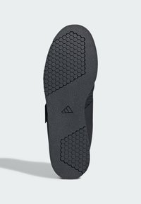 Czarna gumowa podeszwa buta z teksturowanym heksagonalnym wzorem, gładkimi obszarami i detalem logo. Całkowity kształt jest płaski i szeroki.