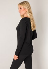 Black long-sleeve top made of soft material, featuring a relaxed fit and seamless design, paired with black leggings in a side profile view.