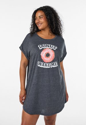 Kobieta z kręconymi włosami uśmiechająca się, ubrana w ciemnoszarą oversize sukienkę typu T-shirt z różowym pączkiem i słowami "Donut Wake Me."