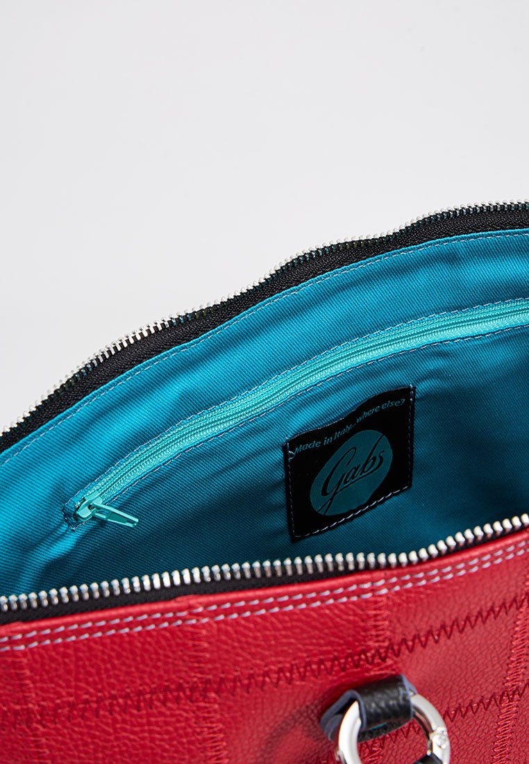 Bolso de cuero rojo parcialmente abierto que muestra un interior de tela azul brillante con un pequeño bolsillo con cremallera y una etiqueta de la marca "Gabs".