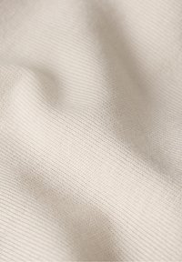 Tessuto beige chiaro con una texture liscia e lavorata a maglia. Righe sottili creano un motivo uniforme sulla superficie del tessuto.