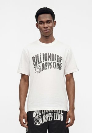 Νέος άνδρας που φοράει λευκό μπλουζάκι Billionaire Boys Club και μαύρο σορτς με αντίστοιχα σχέδια λογότυπου, στέκεται μπροστά σε μια απλή λευκή φόντο.