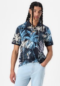 Polo-shirt bleu marine avec un imprimé de feuilles de palmier tropicales et d'oiseaux dans des tons de bleu, doté d'un col classique et de manches courtes.