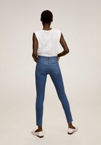 Slanke blauwe denim jeans met een hoge taille, voorzien van twee achterzakken en rafelige zomen. Gepaard met een eenvoudige witte mouwloze top en witte schoenen.