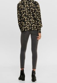 Svart blommig blus med långa ärmar, matchad med grå smala jeans och svarta ankelstövlar. Blusen har ett mönster av gula och vita blommor.