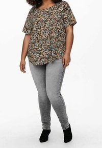 Blommig topp i svart med flerfärgade blommor, kombinerad med grå smala jeans och svarta ankelstövlar. Löst passform och korta ärmar.