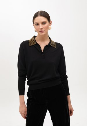 Maglione nero con colletto button-down decorato con borchie dorate. Maniche lunghe, design aderente, realizzato in materiale morbido, abbinato a pantaloni neri plissettati.