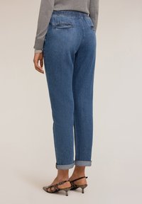 Pantalones de mezclilla azul con un corte relajado, cinturilla elástica, dos bolsillos traseros y puños enrollados. El material tiene un acabado texturizado.