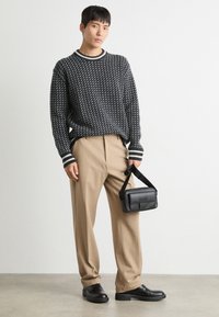Jersey de punto a rayas en negro y blanco con puños de canalé, pantalones beige de corte entallado, zapatos de cuero negros y un pequeño bolso negro.