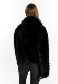 Sort faux fur jakke med cropped design, høj krave og lange ærmer, der har en blød, tekstureret overflade. Sammen med sorte jeans.