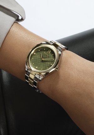 Montre en métal doré et argenté avec un cadran vert à motifs, mettant en avant quatre cristaux, un visage rond et un bracelet à maillons.