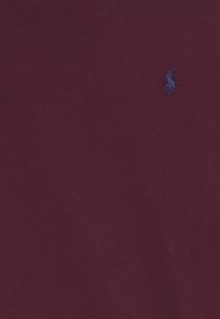 Burgunderröd bomullströja med en liten, broderad blå logotyp. Slät textur, kort ärm och klassisk rund halsdesign.