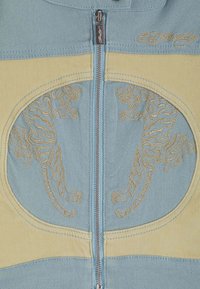 Jeansjacka med en blå och gul design, dragkedjestängning och broderade tigermotiv i guldtråd på frampanelen.