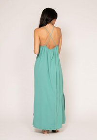 Robe longue et fluide en turquoise clair, dotée d'un dos froncé, de bretelles croisées et d'une fente de chaque côté pour faciliter les mouvements.