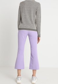 Zwart-wit gestreepte trui met lange mouwen, gecombineerd met lavendelkleurige flared broek. Schoenen zijn zilveren sneakers. De achtergrond is effen.
