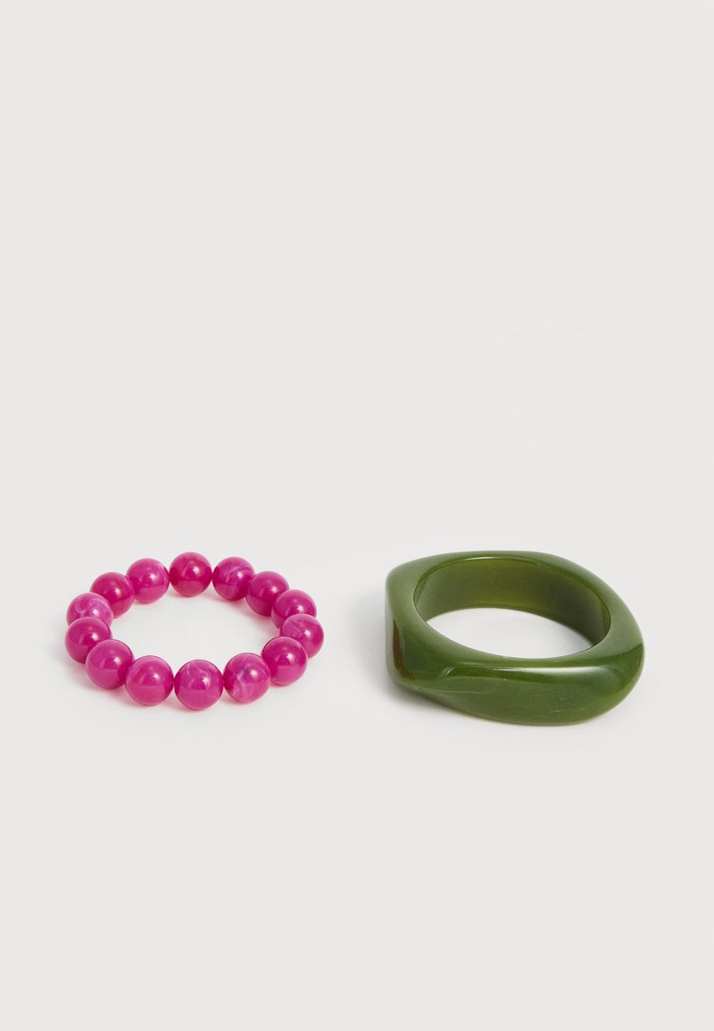 Bracelet à perles rondes roses à côté d'une bague carrée épaisse vert olive lisse sur fond blanc.