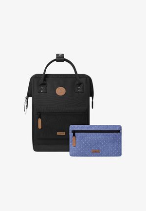 Zwarte canvas rugzak met leren accenten en een voorvak, gecombineerd met een blauwe stippenpouch. Beide hebben ritsen en handvatten.