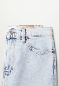 Jean en denim bleu clair plié montrant une poche avant, un bouton, des passants de ceinture et une étiquette de marque sur fond blanc uni.