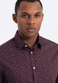 Bordeaux knoopshirt met een wit bloemenpatroon, met een klassieke kraag, lange mouwen en witte knopen aan de voorkant.