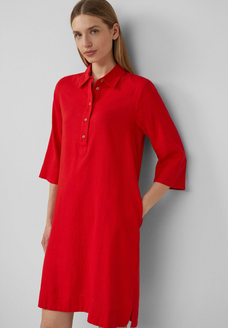 Rotes Leinenkleid mit Kragen, Dreiviertelärmeln, Knopfleiste und seitlichen Schlitzen. Angenehme Textur und knielanges Design.
