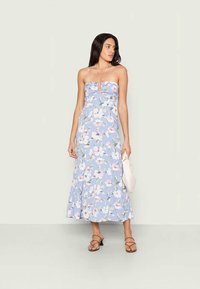 Vestido maxi sem mangas em azul claro, com corpete ajustado e bainha rodada, adornado com padrões de flores brancas e rosas. Acentuado com um colar.