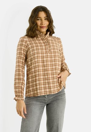 Blusa abotonada a cuadros en beige, marrón y crema con cuello alto, puños fruncidos y un ajuste holgado. Combinada con jeans grises.