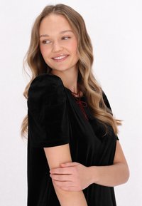 Top din catifea neagră cu mâneci scurte tip volan, decolteu rotund și detaliu cu dantelă din mărgele roșii. Textură fină și croială lejeră.