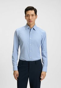 Camicia azzurra a quadri con maniche lunghe, colletto button-down e bottoni bianchi. Abbinata a pantaloni navy scuri. Tessuto dalla consistenza liscia.