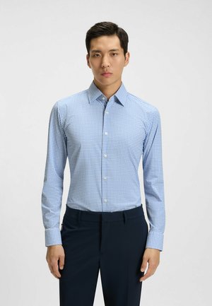 Chemise à carreaux bleu clair avec des manches longues, col boutonné et boutons blancs. Associée à un pantalon navy foncé. Texture de tissu lisse.