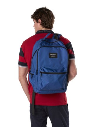 Hombre de espaldas con camisa tipo polo roja y negra, llevando una mochila azul Koroshi con múltiples compartimentos con cremallera.