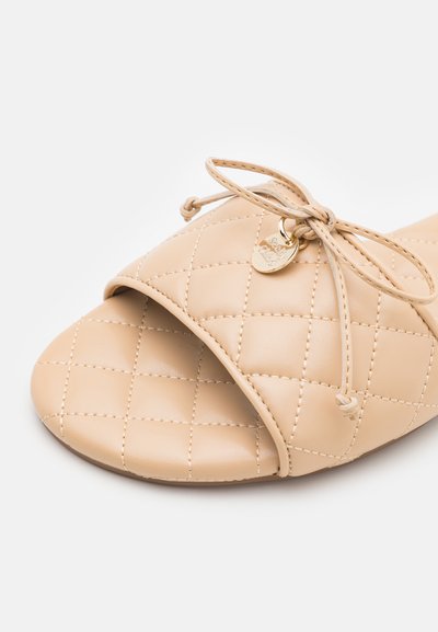 Μπέζ πλεκτό σαγιονάρα με στρογγυλή μύτη, ασημί φιογκάκι και μεταλλικό γούστο. Λείο, συνθετικό υλικό με ραμμένο σχέδιο.