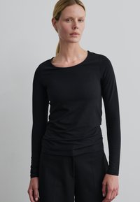 Zwarte langriemtop met een ronde hals, gemaakt van een zachte, stretchy stof. Soepele textuur met een aansluitende pasvorm.